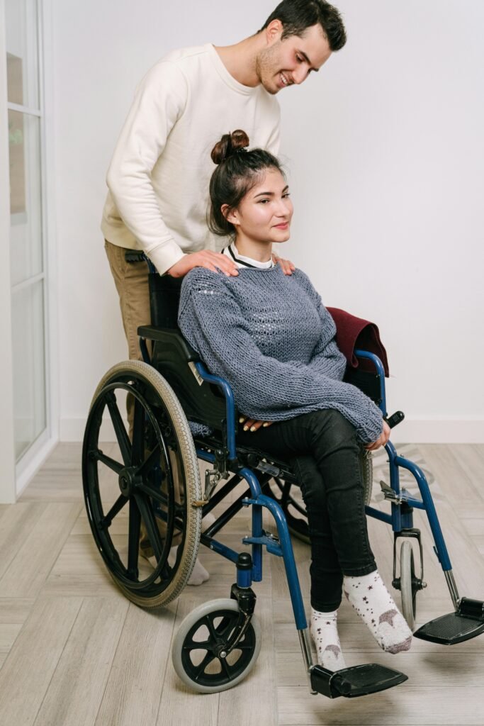 Young man supporting a woman in a wheelchair indoors, showing care and companionship.